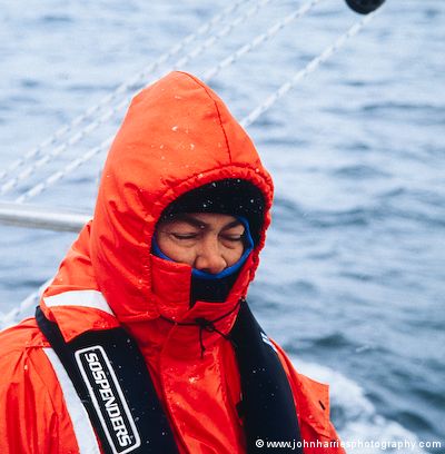 James, crew member on aluminum expedition sailboat Morgan's Cloud, wears a Mustang exposure suit and Sospenders lifejacket in the snow during a passage from West Greenland to Baffin Island