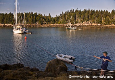Pulling in the dinghy that is tied to the shore fast off the stern of Morgan's Cloud to keep her from swinging into the sailboat moored close by at The Mud Hole, Great Wass Island, Maine