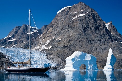 "Morgan's Cloud", a McCurdy and Rhodes 56' cutter, seen beside an arch berg with glacier and mountain behind, a typical East Greenland scene.  The icecap reaches down to the sea in numerous glaciers and there are a floating profusion of bergs and smaller pieces of ice to be carefully avoided.