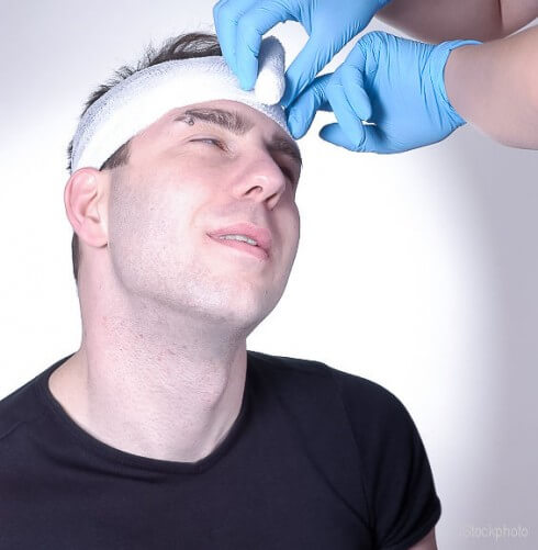 Man with bandage around head and blue gloved hands unrolling bandage iStock_000000579262Small