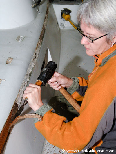 Phyllis uses a chisel and 5-lb maul to chip away the varnished eyebrow on aluminum sailboat Morgan's Cloud