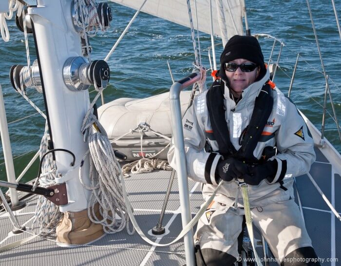 We reef and handle all halyards at the mast. This results in a lot less friction than leading lines back to the cockpit, less clutter, and you are where you need to be if anything jams. Note the substantial granny bars to lean against. Phyllis is clipping on to one of two safety tethers that we keep permanently attached at the mast, prior to un-clipping from the tether that runs on the jack line.