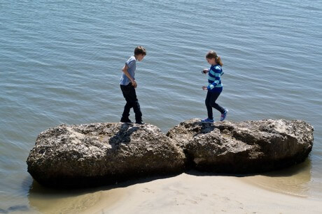 Two young children play on rocks on the seashore