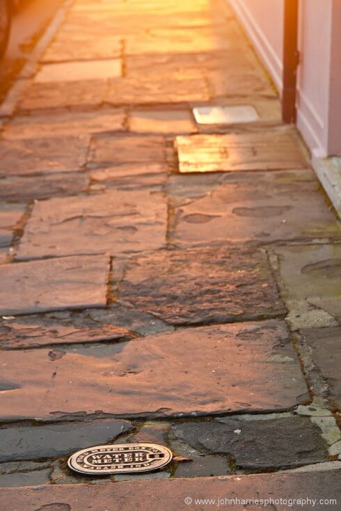 Like many old cities, Charleston has wonderful street surfaces. It's part of the city, so show that, but make it interesting. This may look like a snapshot but it's anything but. Long morning light gives dramatic colour, but even more importantly, the low angle side lighting shows the texture of the flag stones. I placed the inspection cover to anchor the shot and the drain pipe to pull your eye through it.