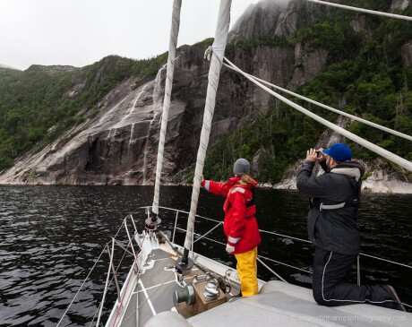Sarah and Ryan on bow of sailboat Morgan's Cloud looking at waterfall in White Bear Bay, Newfoundland
