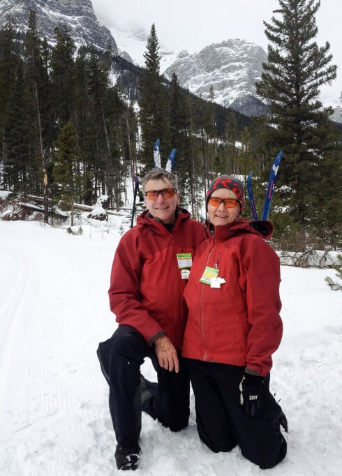 Man and woman kneeling in snow in front of skis and mountains JHH-iphone-6699-20140114