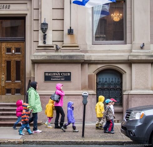 Group of children with two adults walking by Halifax Club on a rainy day